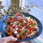 En kebabtallrik med kött, pommes frites, sås och grönsaker på en blå tallrik.