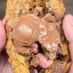 En person håller en kladdkakecookie med smält choklad inuti, som är delad på mitten.