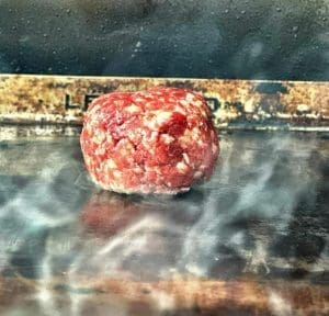 En rå köttfärsbulle som ligger på en grillplatta med rök som stiger upp.