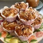 En tallrik med muffins toppade med nötter och äppelbitar i pappersformar.