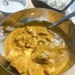 En skål med butter chicken i en krämig sås, serverad med ris och en skål med vit sås.