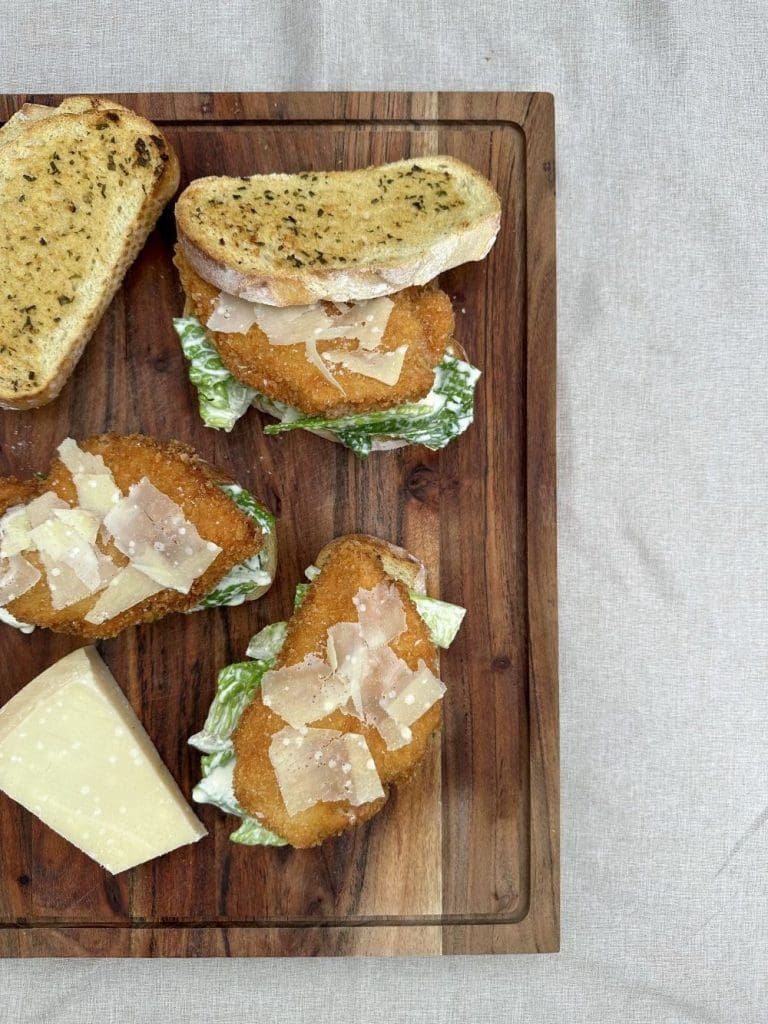 Chicken slider buns 12 Tre Caesarsalladmackor med krutonger och parmesanost på en träskärbräda.