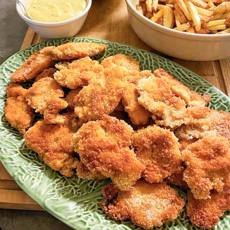 Birijan 9 En tallrik med friterade kycklingnuggets i olika former och storlekar, serverade med sås.