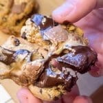 En person håller en del av en chokladchip-kaka med smält Dumle inuti.