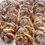 Rader av kanelbullar med pärlsocker på toppen, placerade på en vit yta.