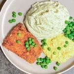 Panerad fiskfilé serverad med potatismos och gröna ärtor på en tallrik.