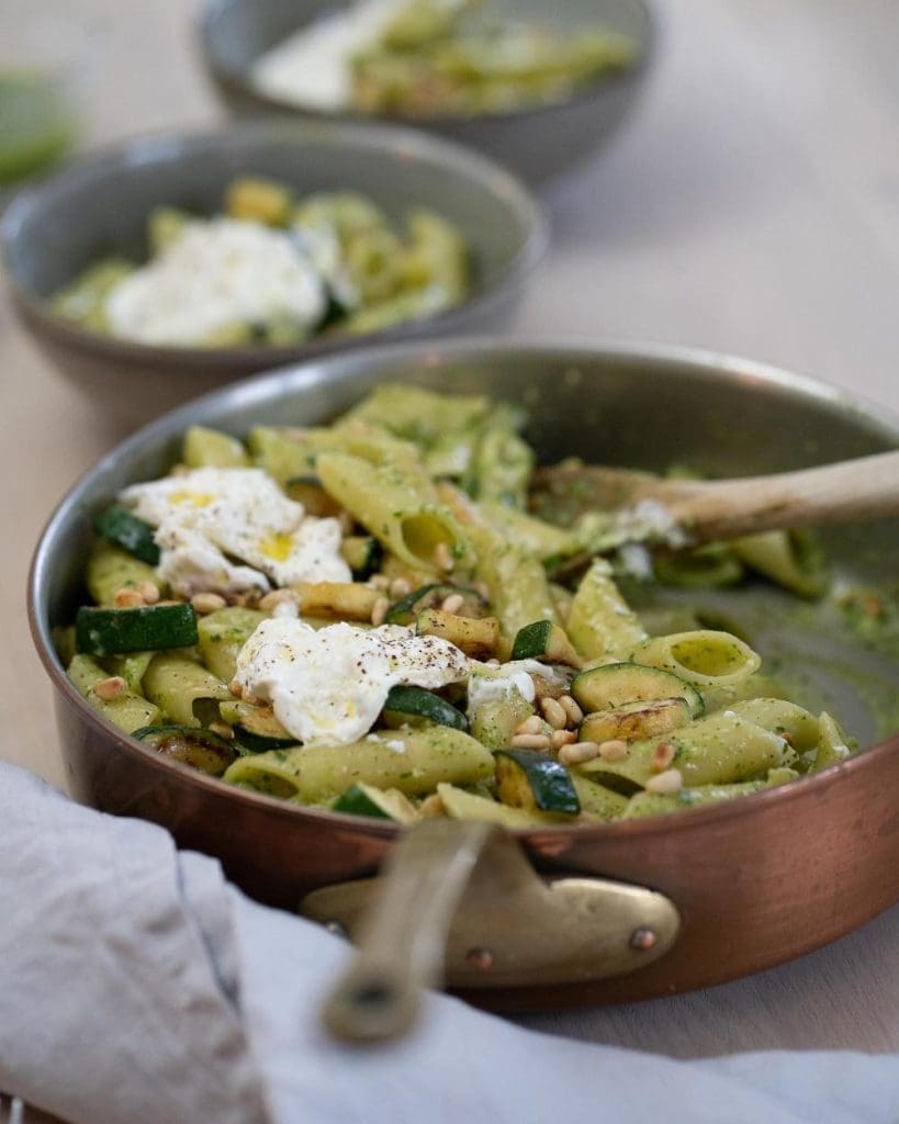 Tryffelpasta med ryggbiff 13 En skål med pasta, pesto, zucchini och pinjenötter i en metallpanna med en träsked.