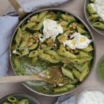 En skål med pasta, pesto, zucchini och toppad med burrata och pinjenötter.