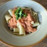 En skål med pasta och tomatsås toppad med färsk basilika.