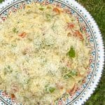 En skål med pastasallad som innehåller grönsaker och riven ost på toppen.
