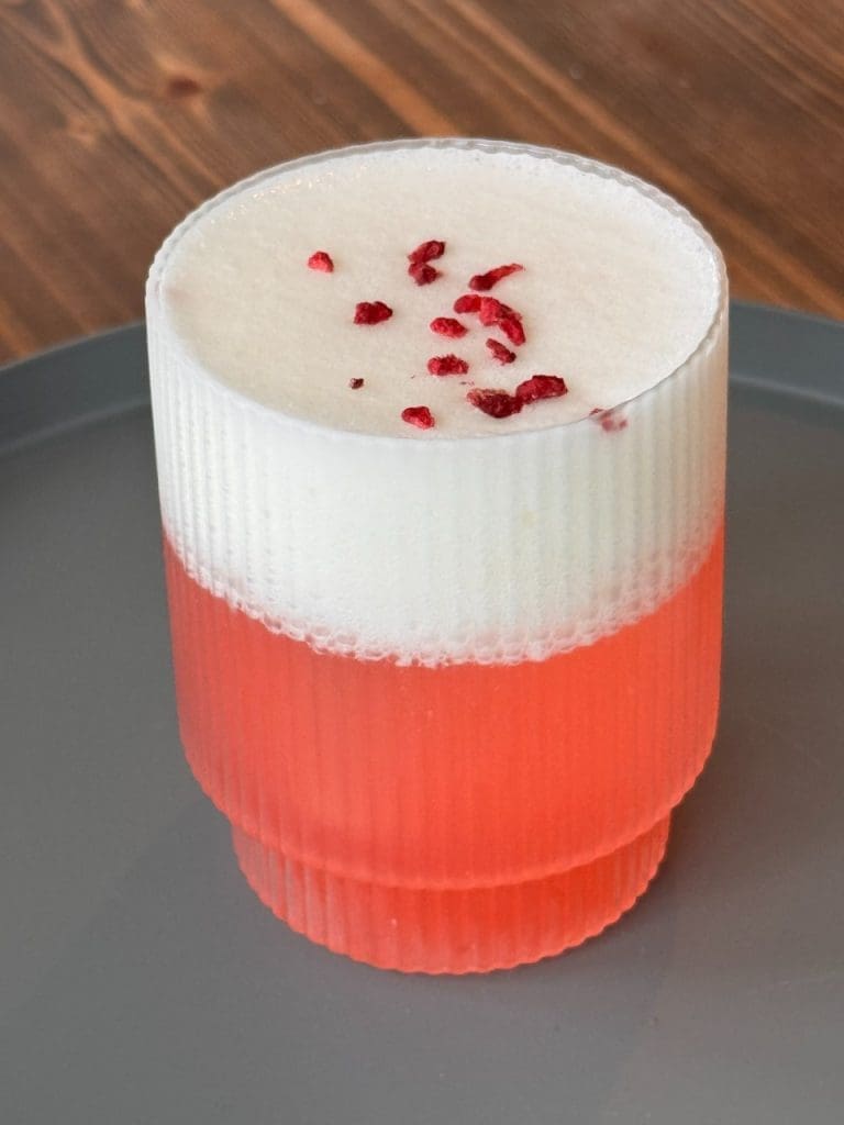 Amaretto sour 9 En drink med lager av rosa vätska och vit skum, dekorerad med torkade hallon på toppen.