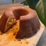 En sockerkaka med brynt smör, delvis skuren, på en skärbräda med en växt i bakgrunden.