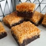 Bit av toscakaka med kokosfyllning och chokladbotten på en vit yta.