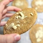 En hand håller en kaka med vit chokladbitar och kanel på en bakplåt.