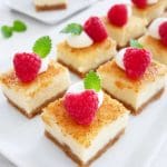 Crème brûlée cheesecake bars topped with raspberries and mint leaves on a white plate.