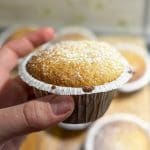 En person håller en fluffig vaniljmuffin med sockerpulver på toppen i handen.