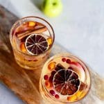 Två glas sangria med frukt, kanelstänger och torkade citrusfrukter på en träskärbräda.