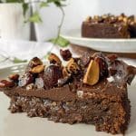 En bit kladdkaka med chokladtopping och hackade nötter på en tallrik.