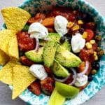En tacobowl med kyckling, avokado, grönsaker och tortillachips på en mönstrad tallrik.