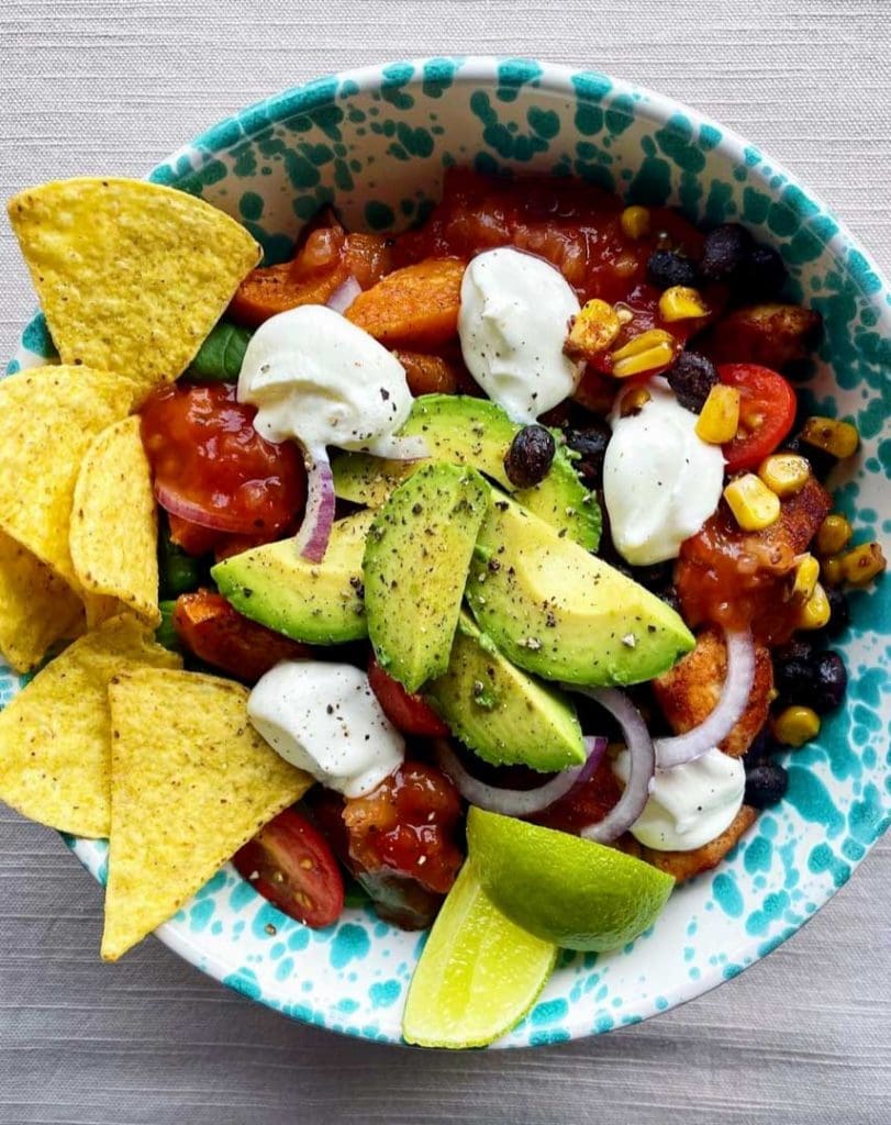 Hot honey halloumi bowl 5 En tacobowl med kyckling, avokado, grönsaker och tortillachips på en mönstrad tallrik.
