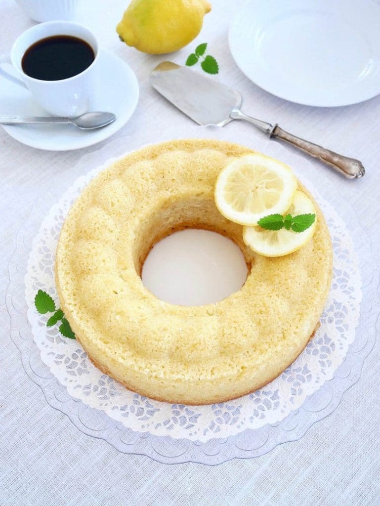 Saftig hallonkaka 7 Citronsockerkaka med citronskivor och mynta på ett vitt fat, med en kopp kaffe i bakgrunden.