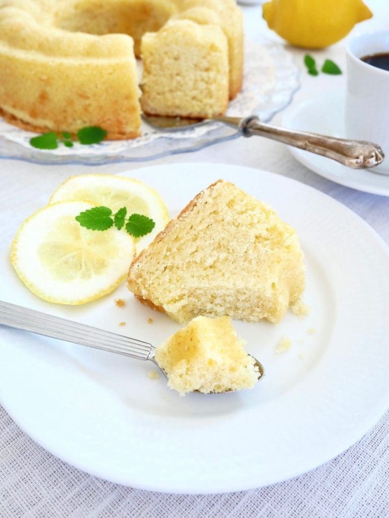 Kardemummakaka 11 En bit citronsockerkaka på en vit tallrik med citronskivor och en gaffel.
