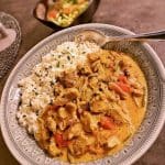 En tallrik med fläskfilégryta i röd curry serverad med ris och grönsaker.
