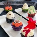 Flera cupcakes dekorerade för Halloween med olika teman och färger på en vit tallrik.