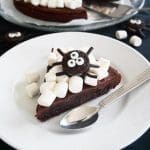 En bit kladdkaka dekorerad med marshmallows och en spindel av kex på en tallrik.