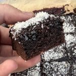 En bit kärleksmums brownie med kokosflingor på toppen, hålls i en hand.