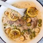 Kycklinggryta med citronskivor, oliver och örter i en gryta med en träsked.
