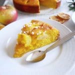 En bit saffranskaka med äpple och apelsin på en vit tallrik med en sked.