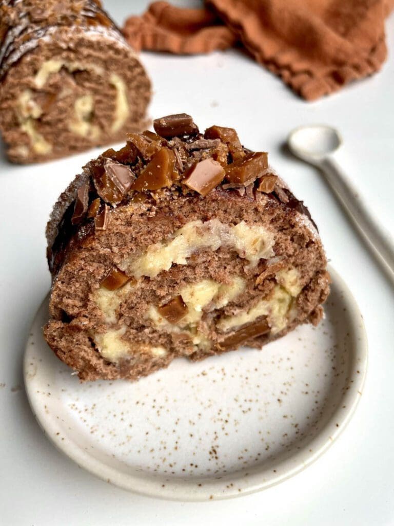 Morotsrulltårta med frosting på brynt smör 11 En skiva av daimrulle med chokladbitar och grädde på en tallrik.