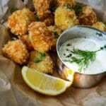 Friterade fiskbitar på en tallrik med dillsås och en skiva citron.