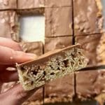 En hand som håller en bit havreruta med nougat ovanför en plåt med fler bitar.