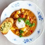 En skål med köttfärssoppa innehållande potatis, grönsaker och en klick gräddfil, serverad med vitlöksbröd.