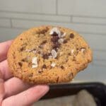 En hand som håller en kaka med chokladbitar och havssalt på ytan.