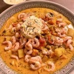 Kramig fisk- och skaldjursgryta med räkor och grönsaker på en tallrik.