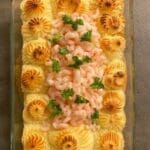 En fiskgratäng med räkor och persilja i en glasform, med gyllene potatismos på toppen.