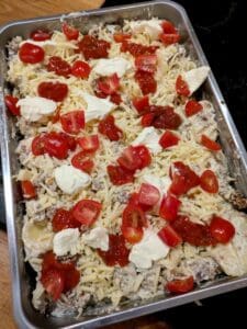 En ugnsform med potatis- och tacogratäng toppad med tomater, ost och sås.