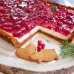 Cheesecake med lingon och pepparkaka, skuren och placerad på en träskiva.