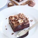 En bit Ferrero Rocher brownie med nötter och choklad på en vit tallrik.