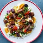En tallrik med potatis, ägg, sill, lök och brödkrutonger på en blå yta.