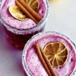 Två glas med rosa dryck dekorerade med torkad citron och kanelstänger.