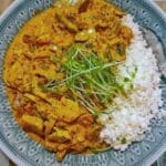 En tallrik med kyckling i röd curry serverad med ris och grönsaker.