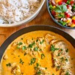En skål med kycklingfilé i currysås, serverad med ris och en fruktsallad.