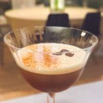 En espresso martini med ett lager skum och kaffebönor på toppen i ett martiniglas.