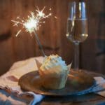 Vaniljcupcake med vit frosting och gnista, placerad på en tallrik bredvid ett glas prosecco.