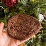 En hand som håller en stor browniekaka med After Eight på en julgranbakgrund.
