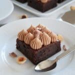 En bit brownie med nougatfrosting och dekorationer av choklad och nötter.